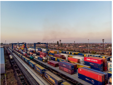 Aerial view of a busy cargo train station with multiple railway tracks and freight trains loaded with various shipping containers.