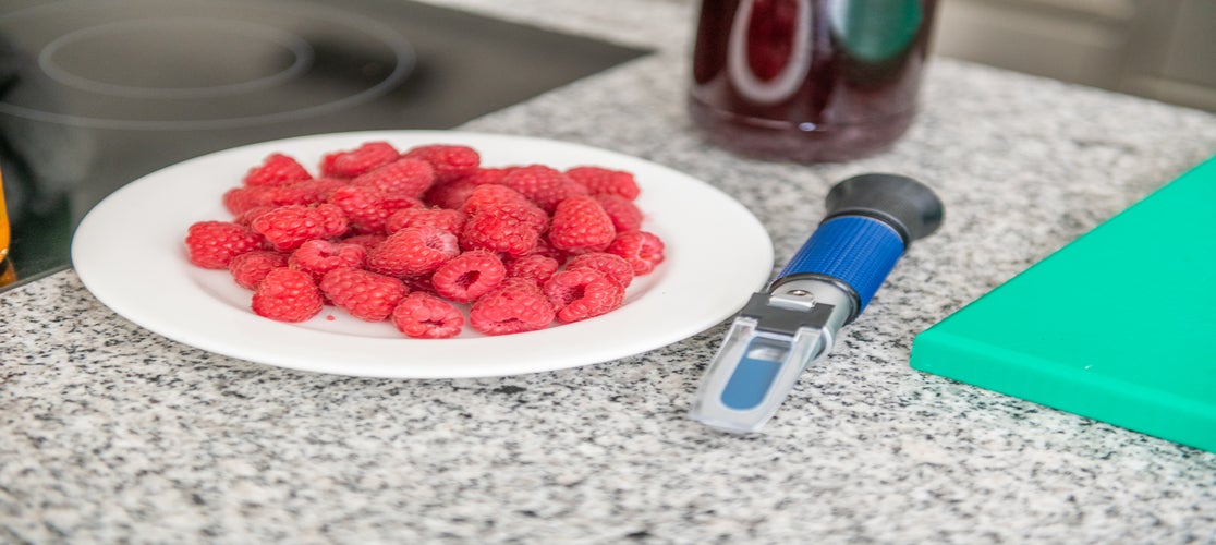 Himbeeren auf einem weißen Teller und im Hintergrund eine Flasche mit Himbeersirup