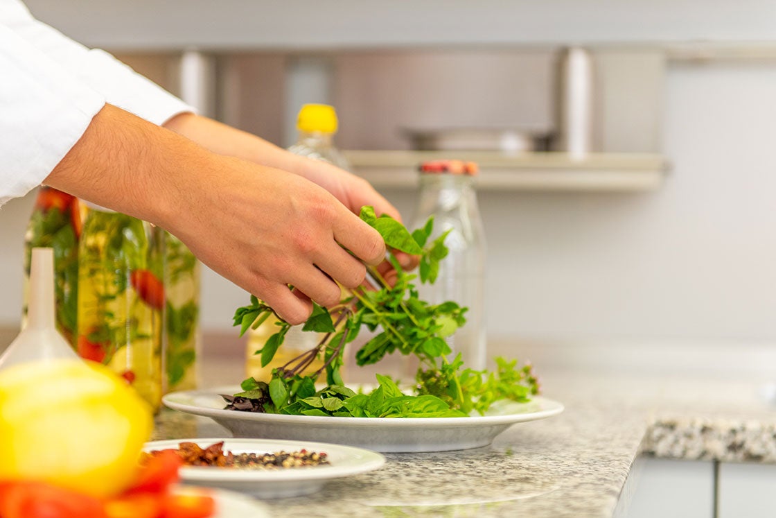 Verschiedene Kräuter werden auf ein Teller gelegt. Im Hintergrund Flaschen mit Kräuteröl