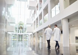 Kilku mężczyzn w białych fartuchach przechadzających się po dużym pomieszczeniu