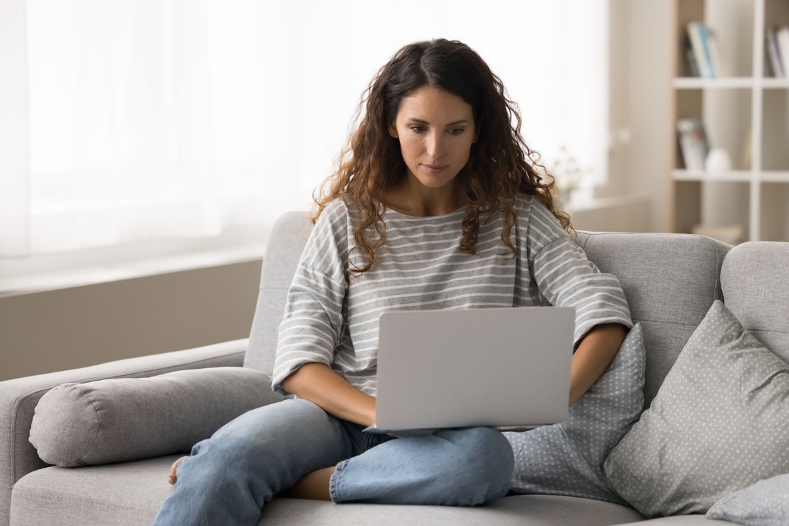 Egy nő ül egy kanapén egy laptopot használva
