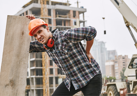 Работник на строеж с предпазна каска, наведен се държи за кръста с болезнено изражение.