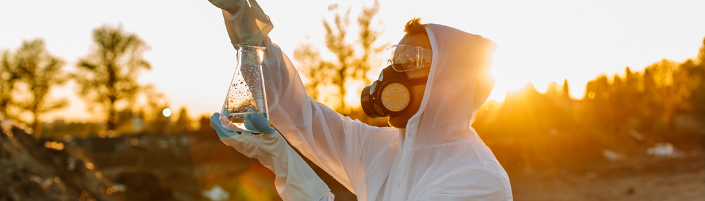 Fehér esőkabátot és védőszemüveget viselő férfi, kezében egy pohárral.