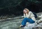 Žena telefonující a sedící na kameni u řeky