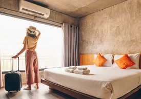 Egy nő áll egy hotelszobában egy bőrönddel...