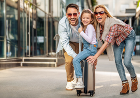 Младо семейство возят на куфар малката си дъщеря и се забаваляват усмихнати.