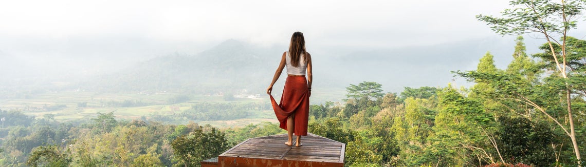 Žena stojící na plošině se stromy a horami v pozadí