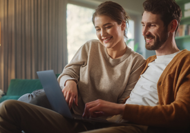 Egy férfi és egy nő ül egy kanapén és nézi a laptopot.