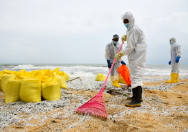 Egy csoport fehér védőruhás ember tisztítja a strandot.