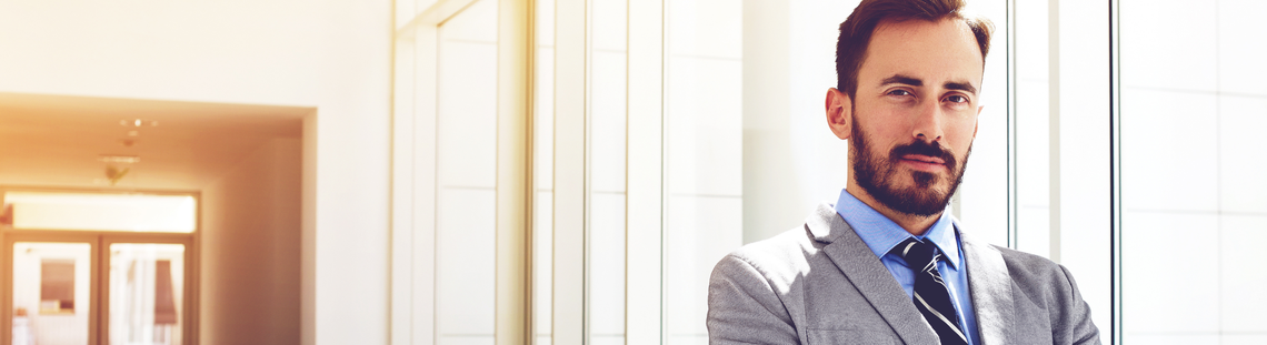 Мъж в костюм стои до прозорец в офис помещение.