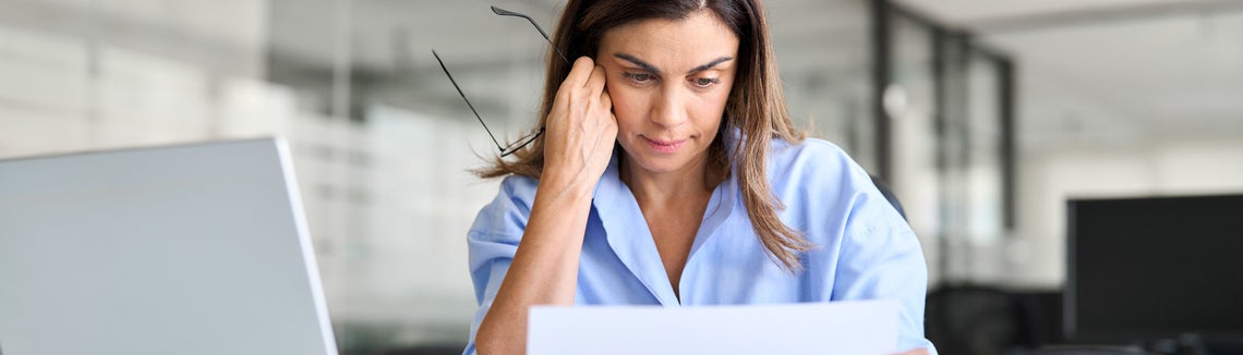 Žena sedí u počítače a dívá se na kus papíru