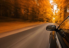 Auto jedoucí po silnici s podzimními stromy v pozadí