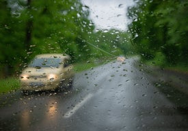 Auto jedoucí po silnici, přičemž na čelním skle se odrážejí kapky deště