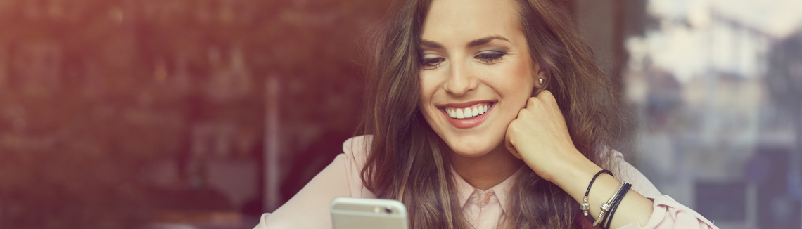 Жена гледа екрана на телефона си и се усмихва.