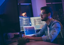 Muž sedící u stolu s několika počítačovými obrazovkami