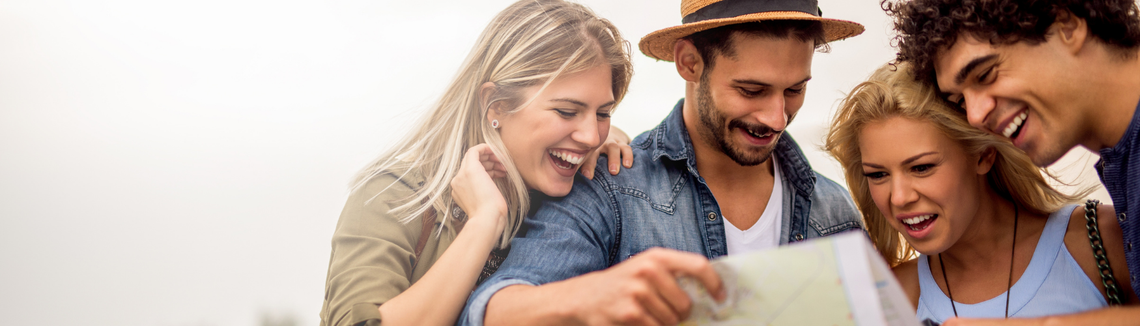 Четирима младежи, двама мъже и две жени, разглеждат пътна карта широко усмихнати