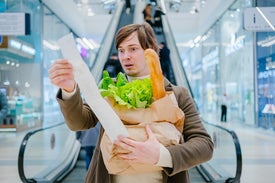 Мъж, който държи торба с хранителни стоки и ужасено гледа касова бележка.