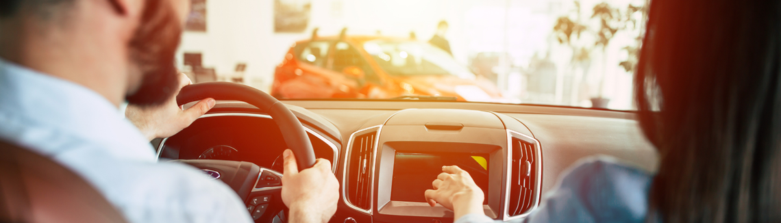 Кадър, сниман от задната седалка на кола, отпред седят мъж и жена, която показва нещо на таблото.