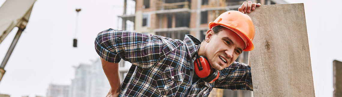 Работник на строеж с предпазна каска се държи за кръста с болезнено изражение.