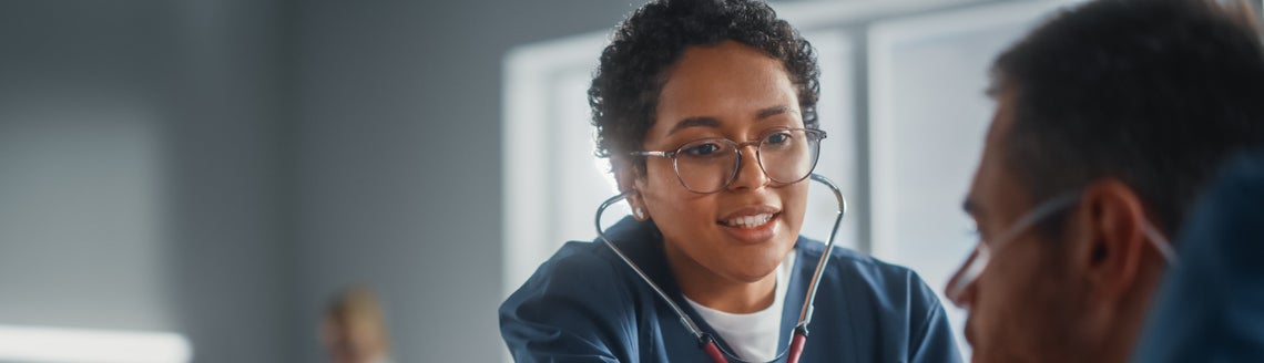 Žena s brýlemi a stetoskopem kontrolující pacienta na lůžku