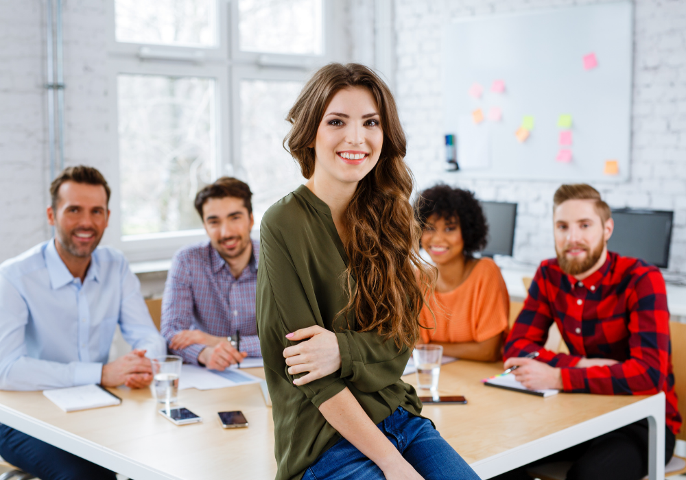 Žena sediaca za stolom, okolo ktorého sú ľudia