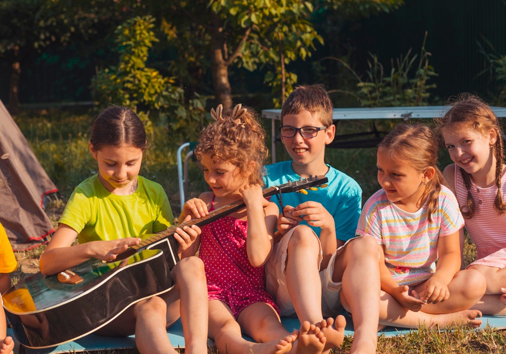 Skupina dětí sedících na dece a hrajících na kytaru