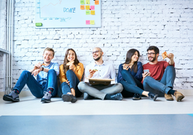 Skupina ľudí sedí na zemi a jedáva