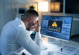 Egy férfi ül egy íróasztalnál egy számítógép képernyője előtt.