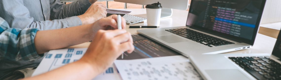 laptopy z wyświetlonymi danymi, wydruki oraz ręce osób pracujących