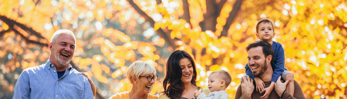 Дядо, баба, мама с бебе, баща с баткото на конче вървят на фона на дървета с есенни жълти листа.