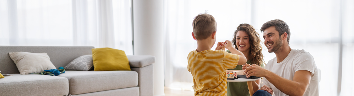 Младо семейство с малкия си син играят настолна игра на холната си маса.