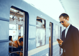 Egy férfi áll egy vasútállomáson, és a telefonját nézi.