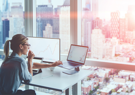 Egy nő ül egy íróasztalnál egy laptop és egy ablakon a városra néző kilátással