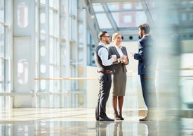 Skupina lidí stojících v místnosti s okny