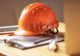 kask ochronny budowlany pomarańczowy na stole z dokumentami