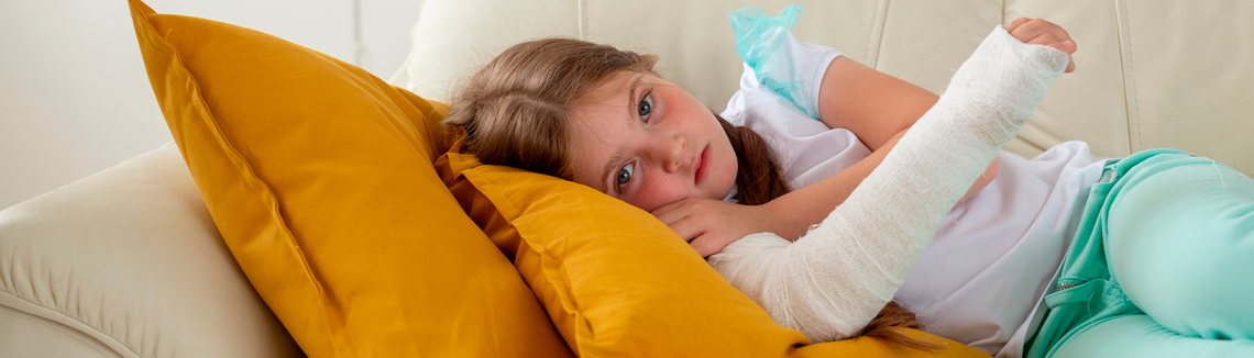 dziewczynka w wieku szkolnym ze złamana ręką leży na kanapie i patrzy w obiektyw