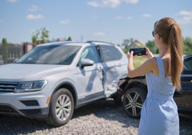 Žena si fotí rozbité auto.