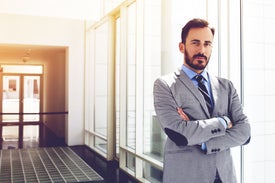 Мъж в костюм стои до прозорец в офис помещение.