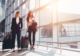 Două femei se plimbă cu bagaje într-o clădire