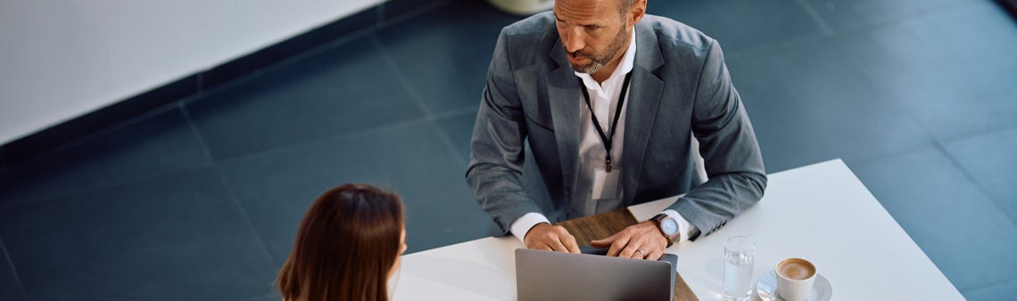 Muž v obleku sedí u notebooku a dívá na ženu 