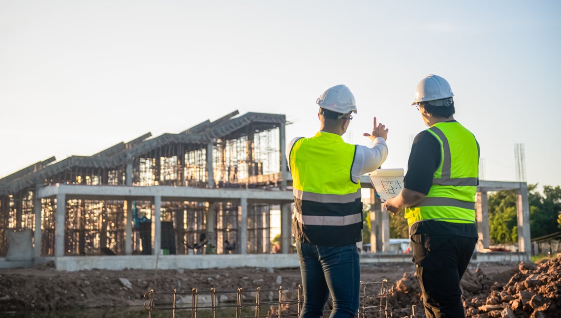 Dvaja muži v bezpečnostných vestách a prilbách na stavenisku
