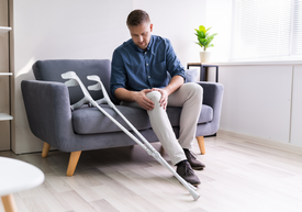 Egy férfi egy kanapén ül egy mankóval.