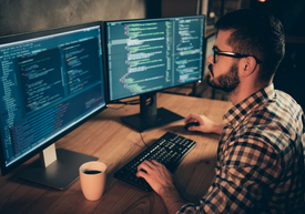 Muž sediaci za stolom s dvoma obrazovkami počítača