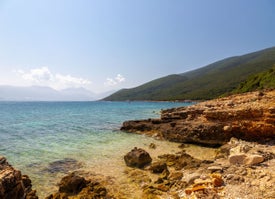 Skalnaté pobřeží s vodní plochou a horami v pozadí