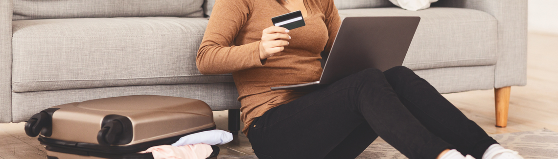 Egy nő ül a földön, kezében egy laptop és egy hitelkártya.