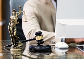 Човек на компютър, до чийто монитор има фигурка на Темида и съдийско чукче.