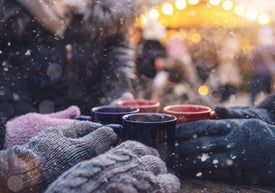 Skupina rukou v rukavicích držících hrnky na adventním trhu