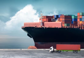 Голям товарен кораб с контейнери на него и пристанище на преден план с камион