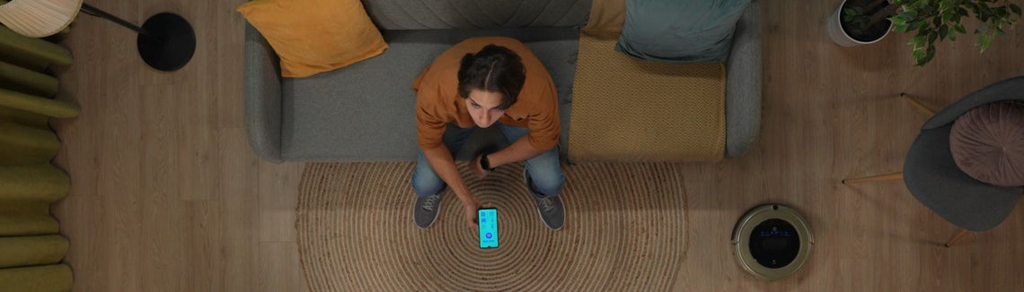 Muž sedící na pohovce, držící telefon a sledující televizi