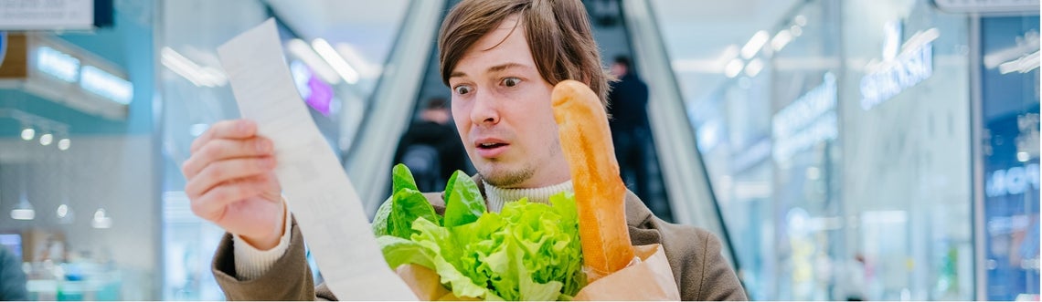 Мъж държи торба с храна и ужасено гледа касова бележка.